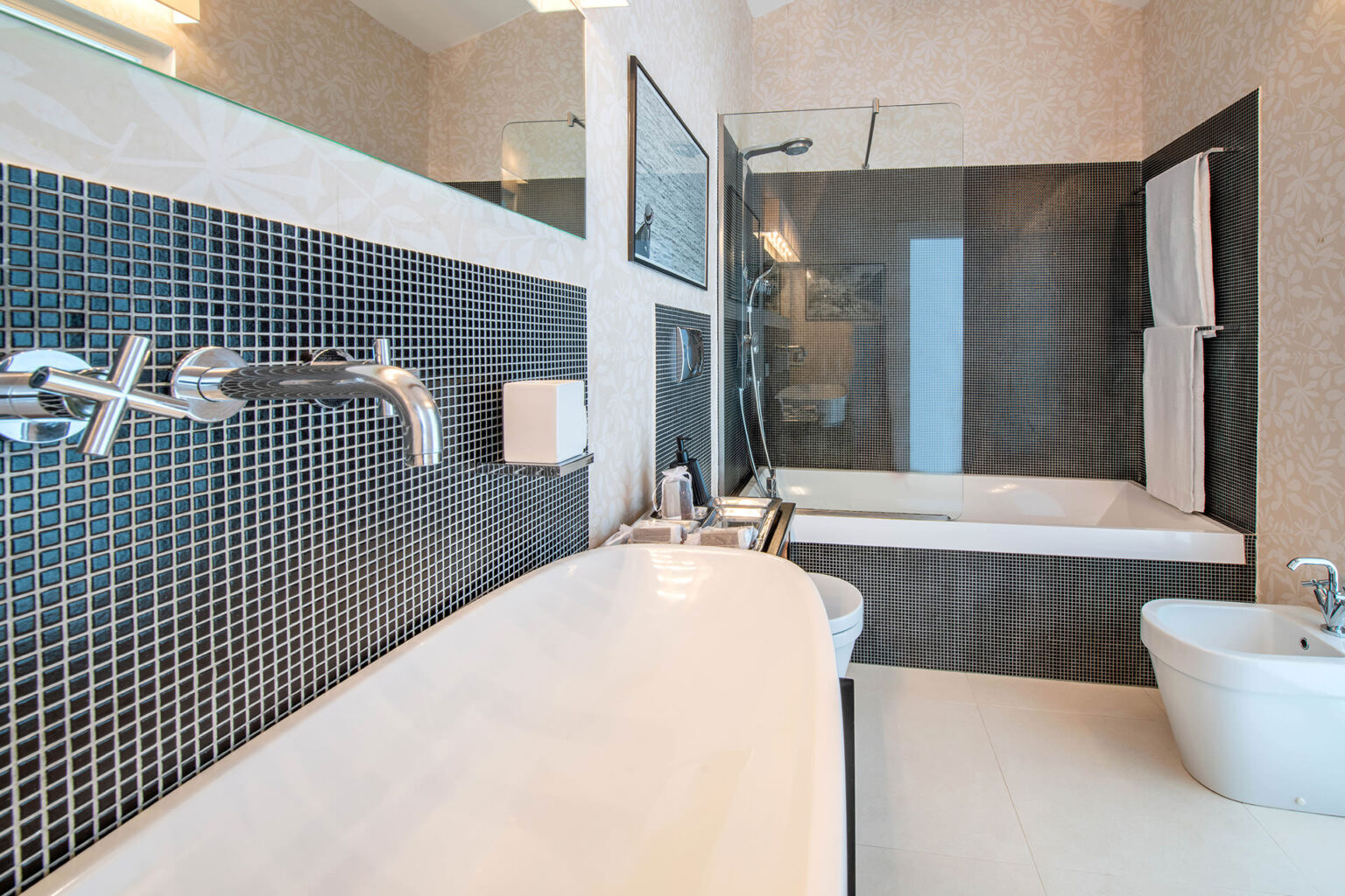 Modern bathroom featuring a sleek white bathtub, stylish faucet, and contemporary black mosaic tiles. The design includes a glass shower enclosure and minimalistic fixtures for an elegant look. | Only on SopranoVillas