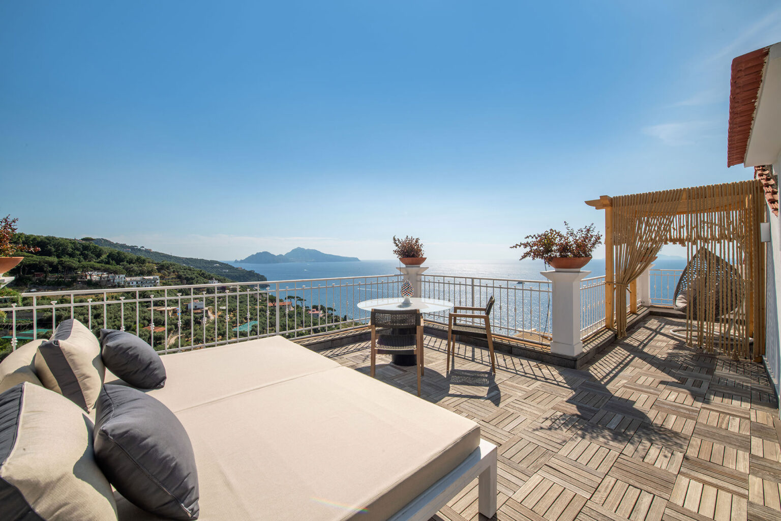 Luxurious terrace with ocean view, featuring a sunbed, dining table, and stylish seating, perfect for relaxation and outdoor dining in a scenic coastal setting. | Only on SopranoVillas