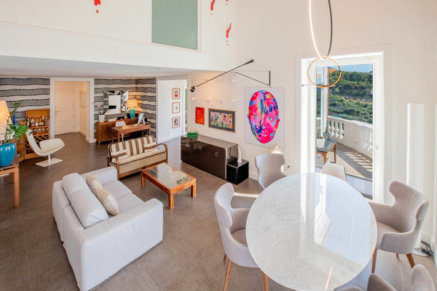 Modern open-concept living room and dining area featuring stylish furniture, contemporary art, and large windows with scenic views. | Only on SopranoVillas