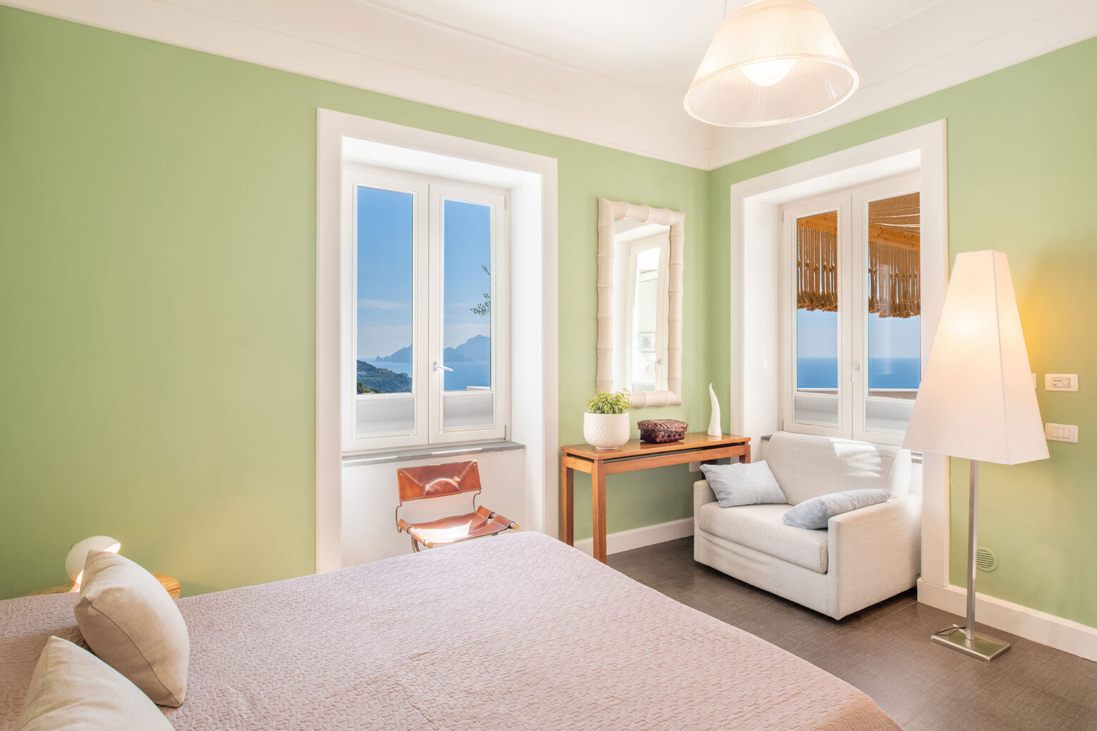 Bright and airy bedroom featuring green walls, large windows with scenic views, a comfortable bed, a cozy armchair, and a stylish lamp, creating a relaxing atmosphere. | Only on SopranoVillas