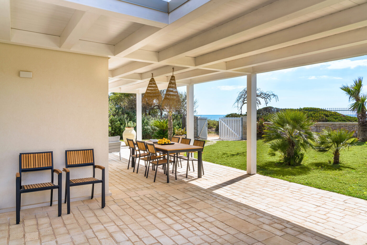 Spacious outdoor patio with wooden dining table and chairs, surrounded by lush greenery and ocean views, perfect for entertaining and relaxation. | Only on SopranoVillas