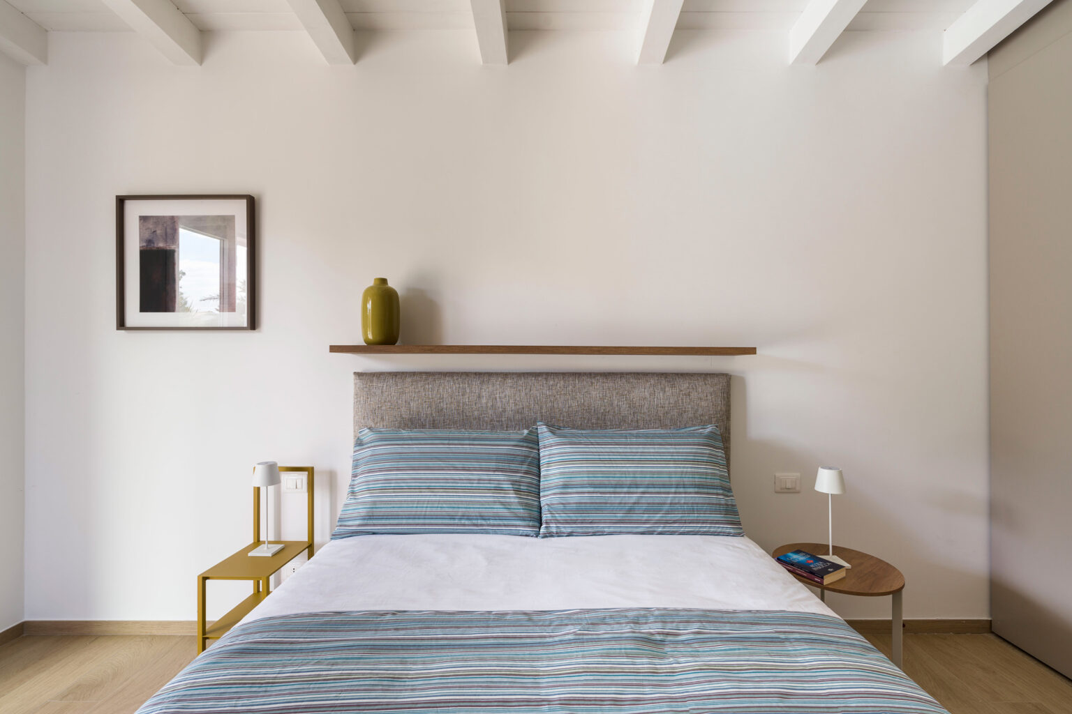 Modern bedroom featuring a comfortable bed with blue and white striped bedding, minimalist decor, wooden accents, and soft lighting. | Only on SopranoVillas