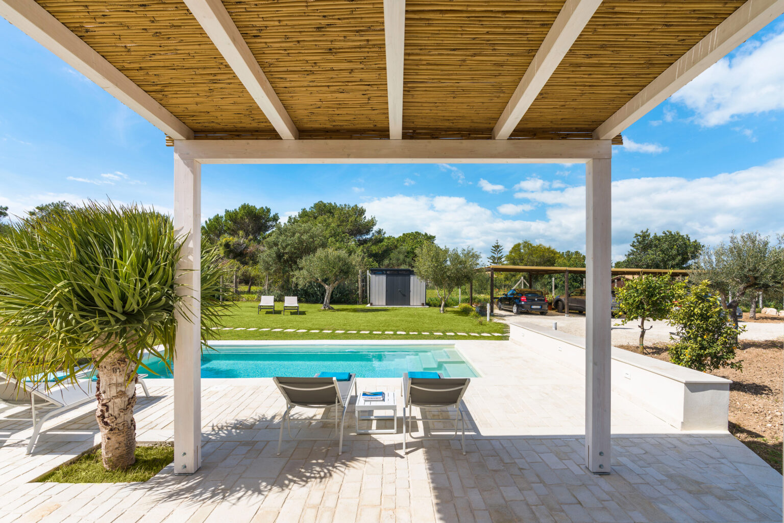 Modern outdoor space featuring a swimming pool, sun loungers, and lush greenery under a blue sky. The image captures a serene and inviting atmosphere, perfect for relaxation and leisure. | Only on SopranoVillas
