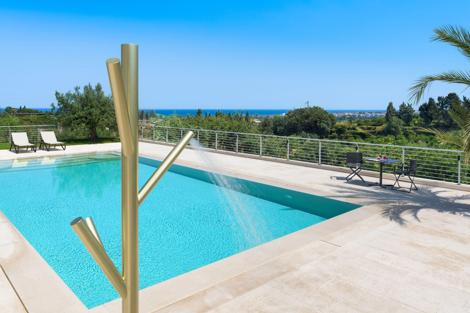 Luxury outdoor swimming pool with a modern water feature, surrounded by lush greenery and a stunning ocean view, perfect for relaxation and leisure. | Only on SopranoVillas