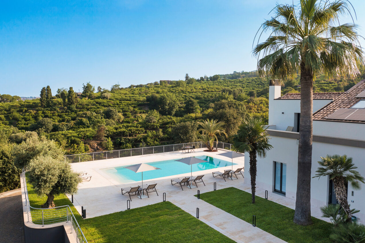 Aerial view of a luxurious villa with a swimming pool surrounded by palm trees and lush greenery, ideal for a relaxing getaway. | Only on SopranoVillas