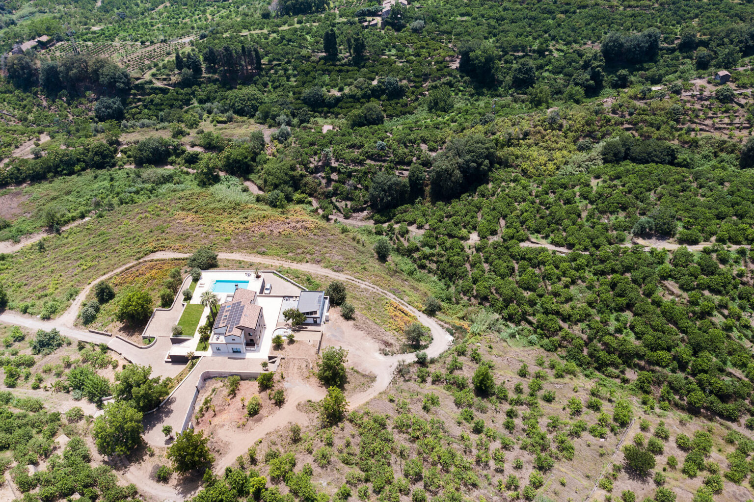 Aerial view of a modern house with a swimming pool surrounded by lush greenery and farmland, showcasing a serene rural landscape. | Only on SopranoVillas