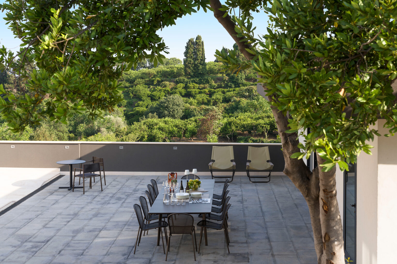 Outdoor dining area featuring a modern table and chairs surrounded by lush greenery, perfect for al fresco meals. | Only on SopranoVillas