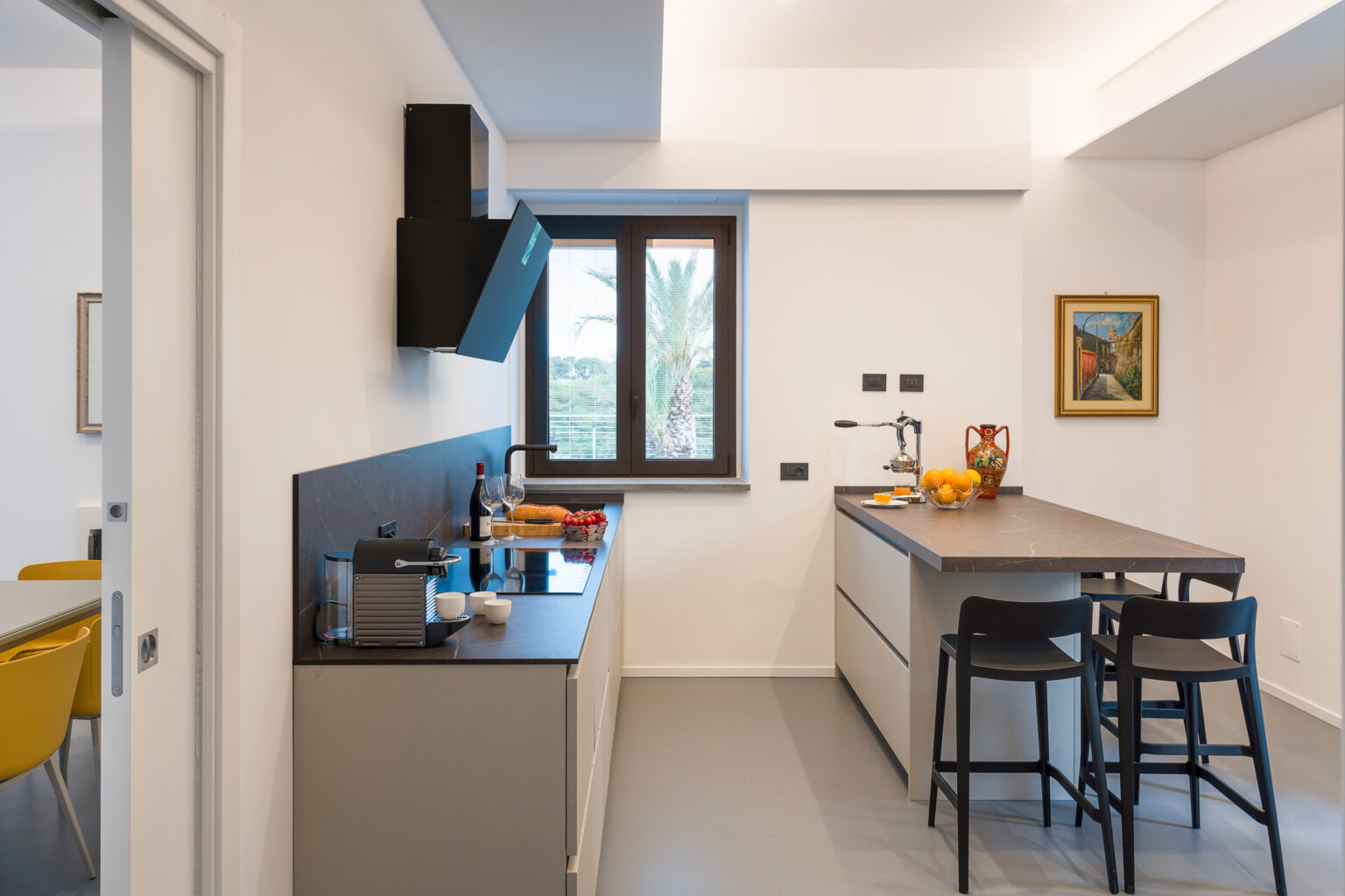Modern kitchen interior featuring a sleek design with a central island, bar stools, and a window providing natural light. The kitchen is equipped with contemporary appliances and stylish decor, creating a functional and inviting space. | Only on SopranoVillas