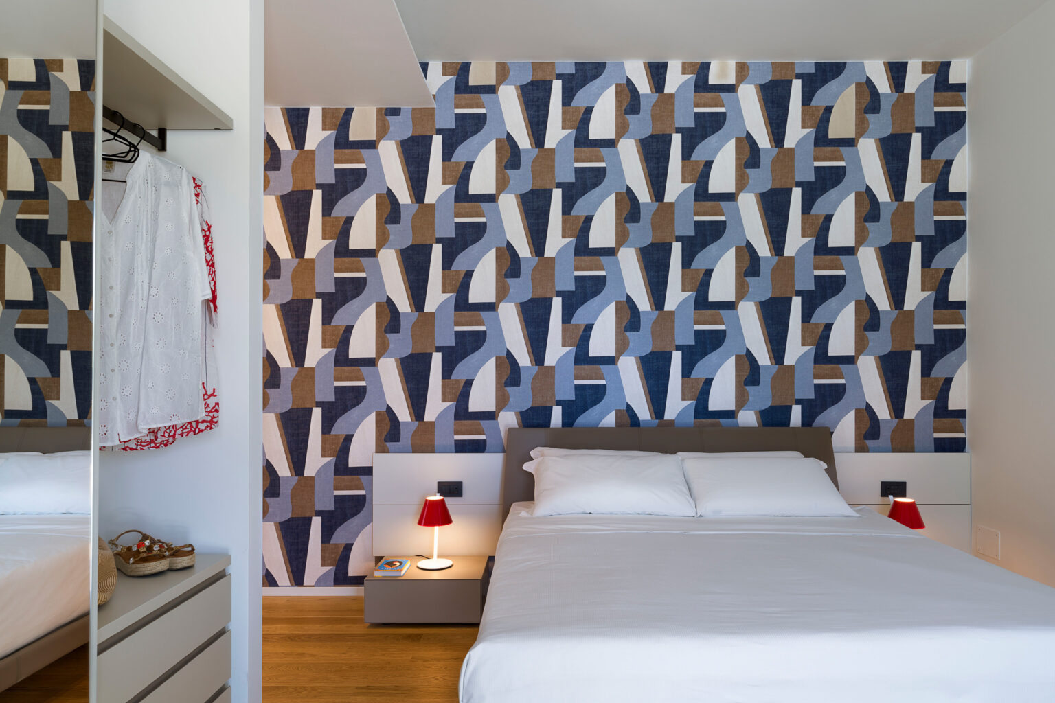 Modern bedroom featuring a patterned accent wall in blue, white, and brown tones, with a comfortable bed, bedside lamps, and a stylish wardrobe. | Only on SopranoVillas