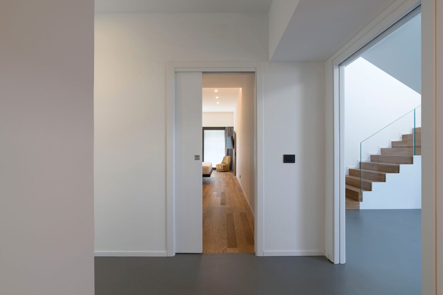 Modern interior hallway featuring a minimalist design, with a view of a spacious living area and a staircase in the background. Natural light illuminates the space, highlighting the sleek lines and neutral color palette. | Only on SopranoVillas