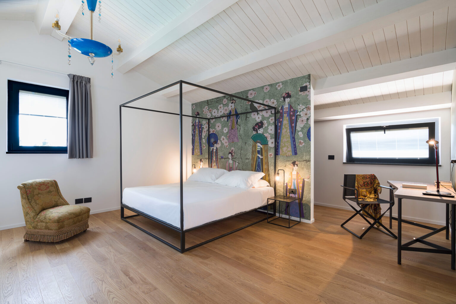 Modern bedroom featuring a four-poster bed, stylish decor with floral wallpaper, a cozy armchair, and a workspace with a desk and chair, all set in a bright and airy atmosphere. | Only on SopranoVillas