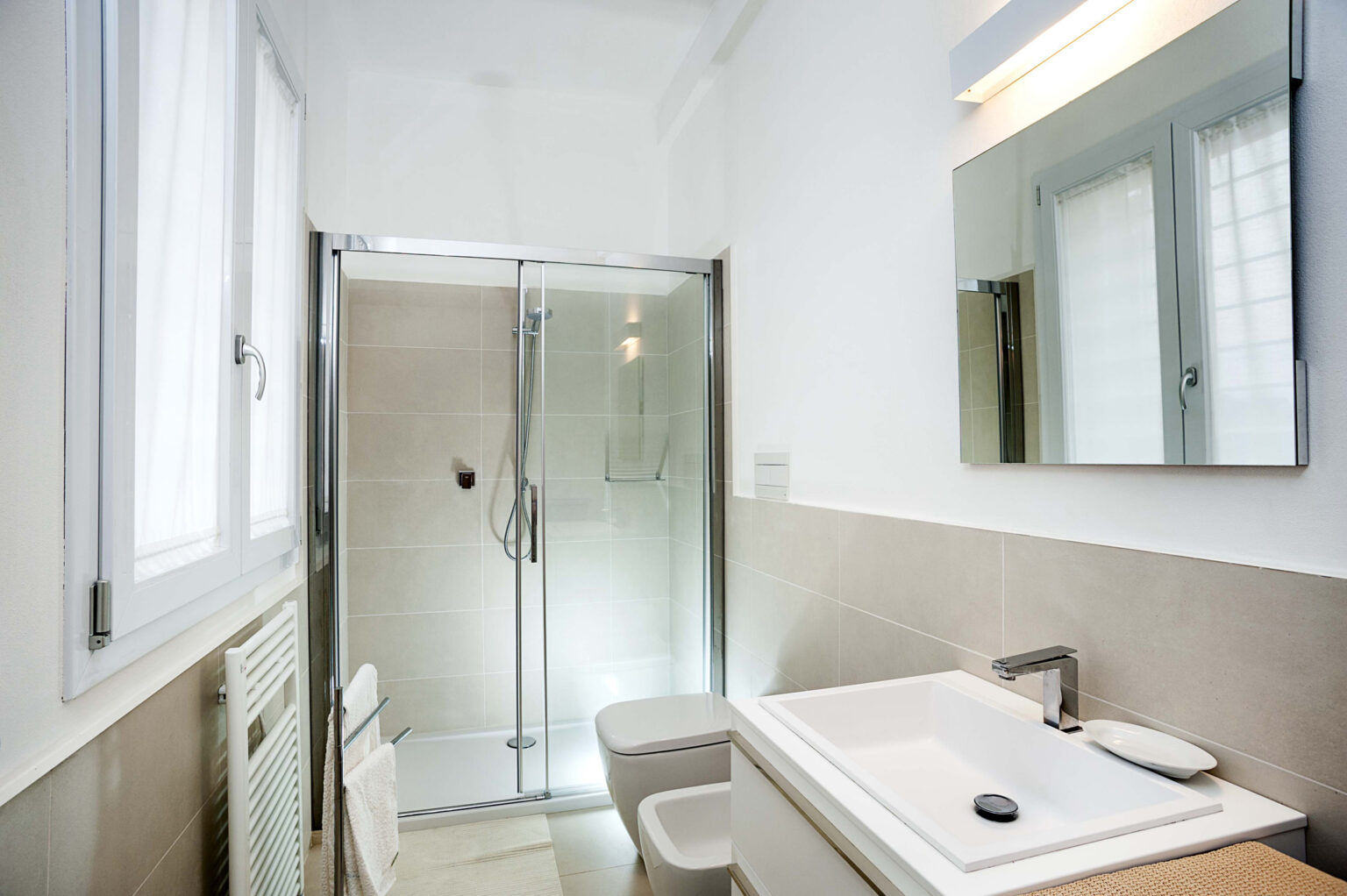 Modern bathroom featuring a glass shower enclosure, sleek sink, and neutral tile design, complemented by natural light from a window. | Only on SopranoVillas
