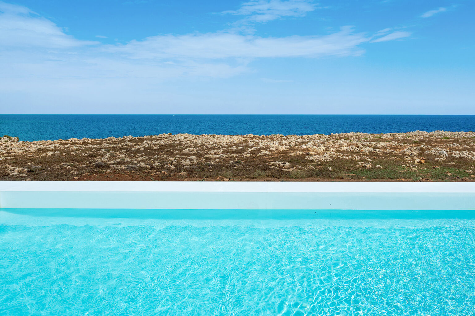 Infinity pool overlooking the ocean with a clear blue sky and rocky coastline in the background. | Only on SopranoVillas
