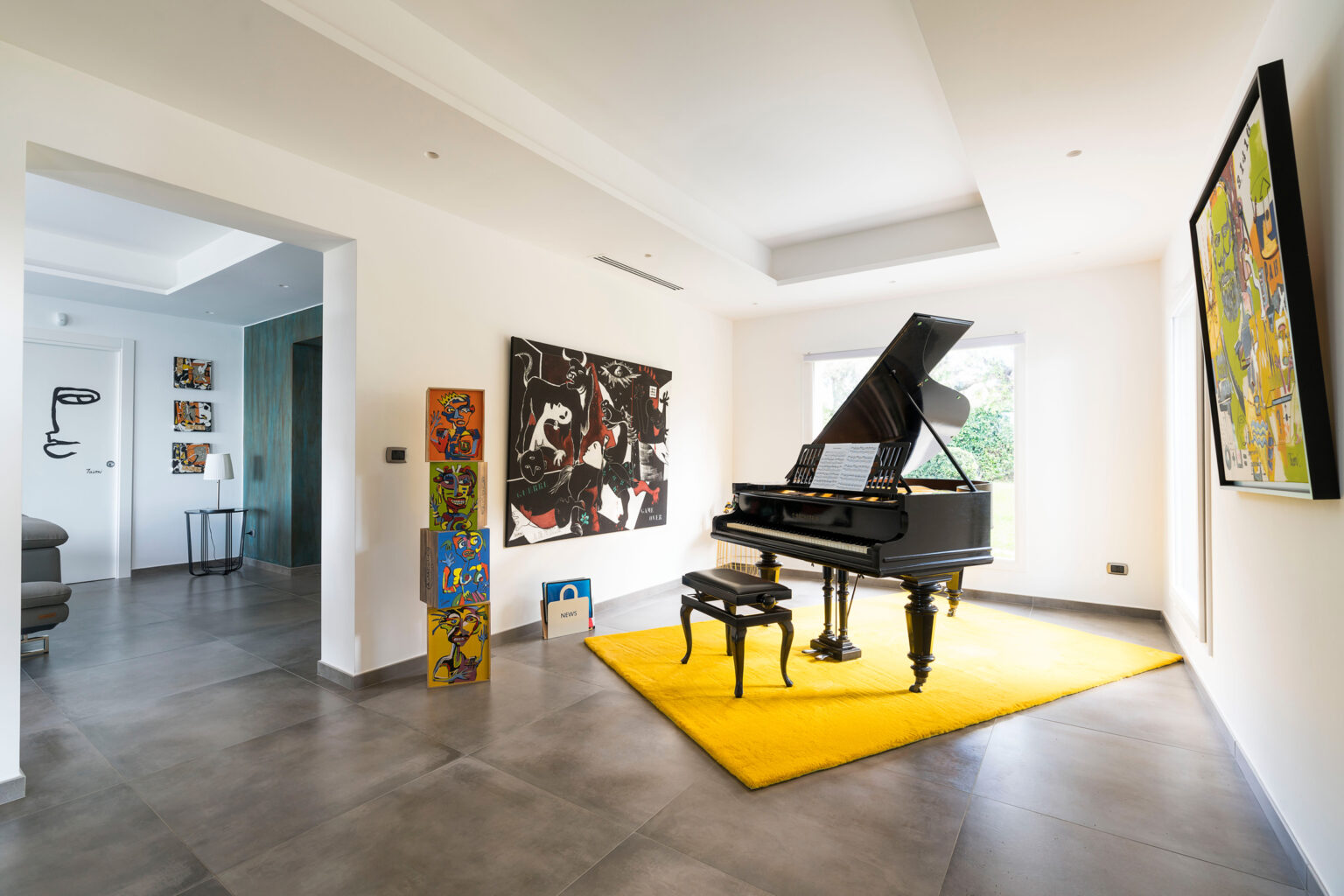 Elegant living room featuring a grand piano on a vibrant yellow rug, surrounded by modern artwork on the walls. The space is well-lit with natural light streaming in from large windows, showcasing a contemporary design aesthetic. | Only on SopranoVillas