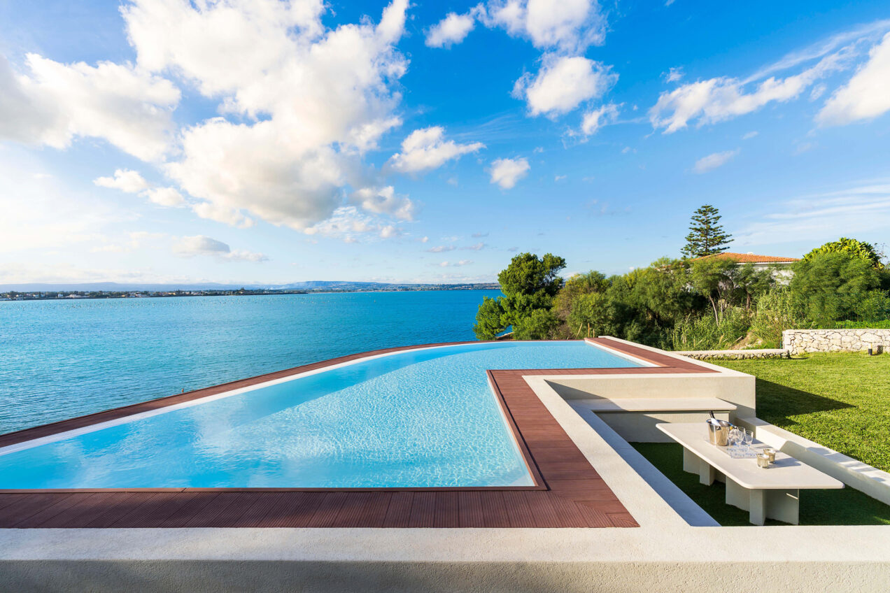 Infinity pool overlooking the ocean with lush greenery and a clear blue sky, ideal for luxury vacation settings. | Only on SopranoVillas