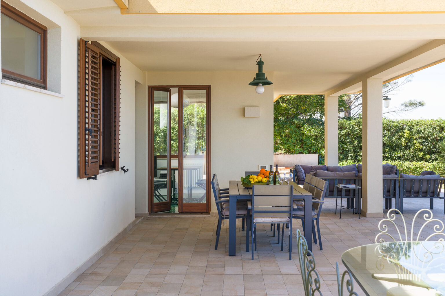 Spacious outdoor patio featuring a dining table with fresh fruit, surrounded by comfortable seating and lush greenery. Natural light enhances the inviting atmosphere, perfect for relaxation and entertaining. | Only on SopranoVillas