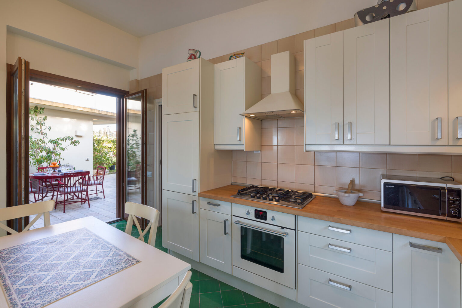 Modern kitchen interior with white cabinetry, wooden countertops, and stainless steel appliances, featuring an open doorway leading to an outdoor dining area. | Only on SopranoVillas