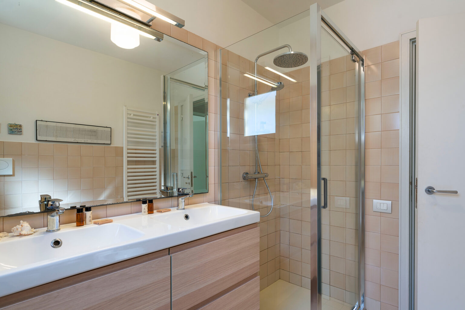 Modern bathroom featuring a double vanity with a white countertop, large mirror, and a glass shower enclosure. The neutral tile and wood accents create a sleek and inviting atmosphere. | Only on SopranoVillas