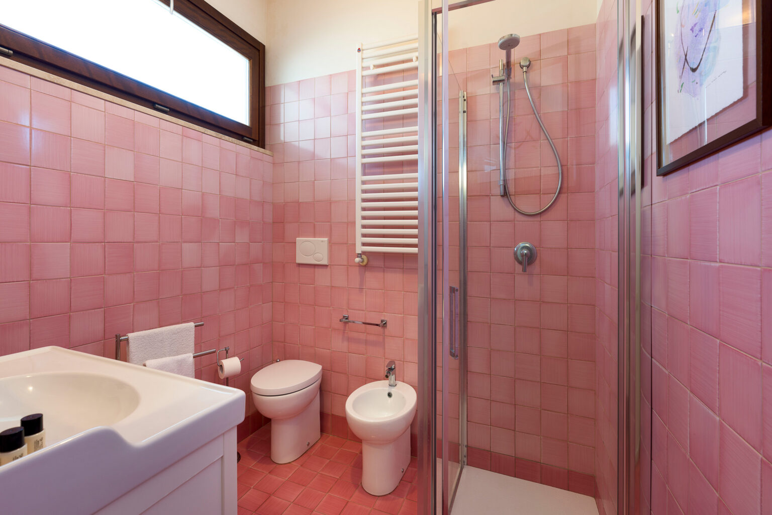 Modern pink tiled bathroom featuring a shower, toilet, bidet, and sink, with natural light coming through a window. | Only on SopranoVillas