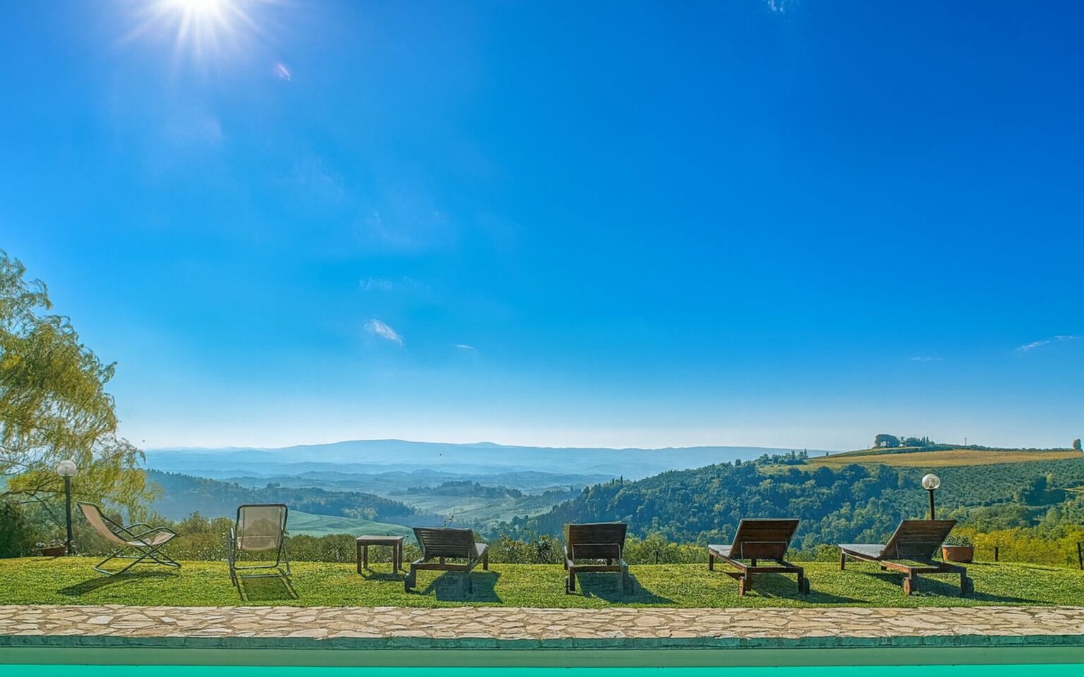Luxurious Italian villa with a stunning panoramic view, featuring sun loungers by the pool under a clear blue sky, ideal for relaxation and vacation rentals. | Only on SopranoVillas