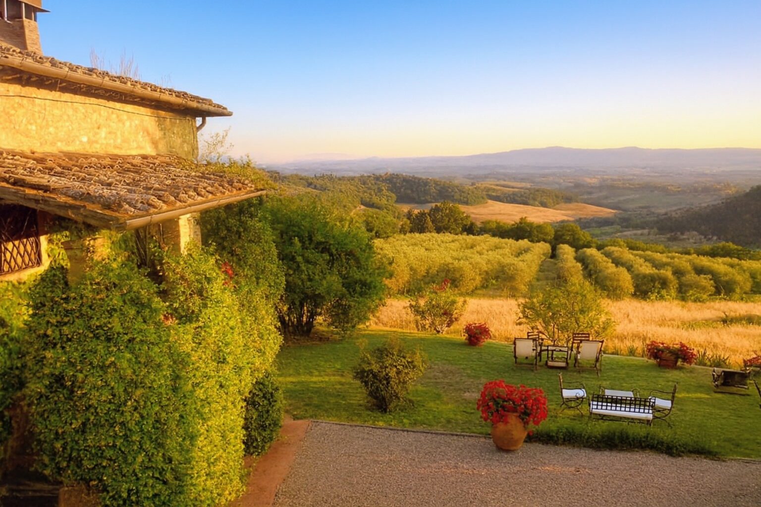 Luxury villa rental in Italy with stunning sunset views over rolling hills and lush greenery, featuring outdoor seating and beautiful landscaping. | Only on SopranoVillas