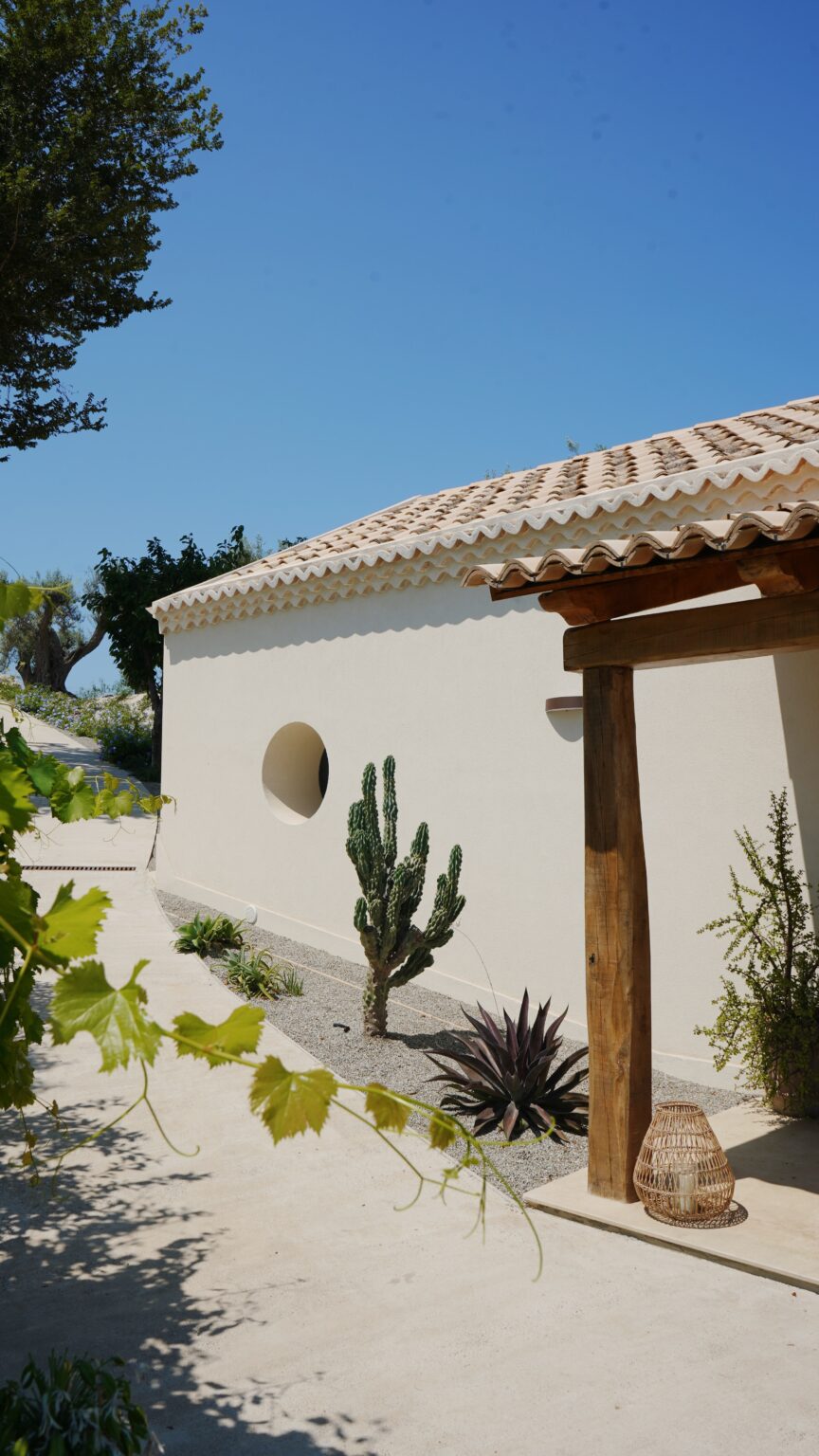 Modern white building with round window, surrounded by cacti and greenery in a sunny outdoor setting. | Only on SopranoVillas