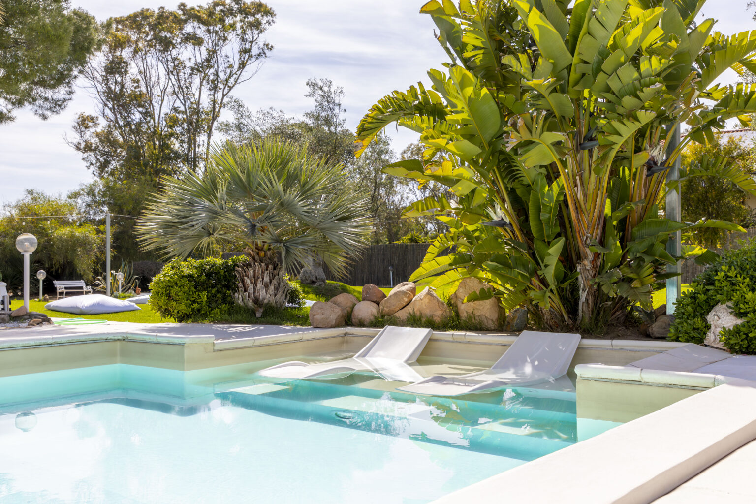Luxury backyard oasis featuring a swimming pool with a water slide, surrounded by tropical plants and rocks, ideal for relaxation and outdoor entertainment. | Only on SopranoVillas