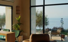 Modern living room with large windows showcasing a serene ocean view, featuring a leather lounge chair, wooden dining table, and indoor plants, illuminated by natural light.