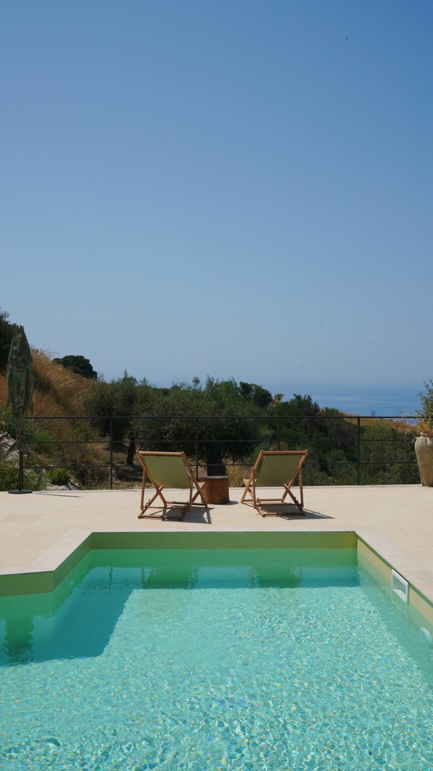 Two lounge chairs on a terrace overlooking a serene landscape with trees and ocean in the background, perfect for relaxation and enjoying the view. | Only on SopranoVillas