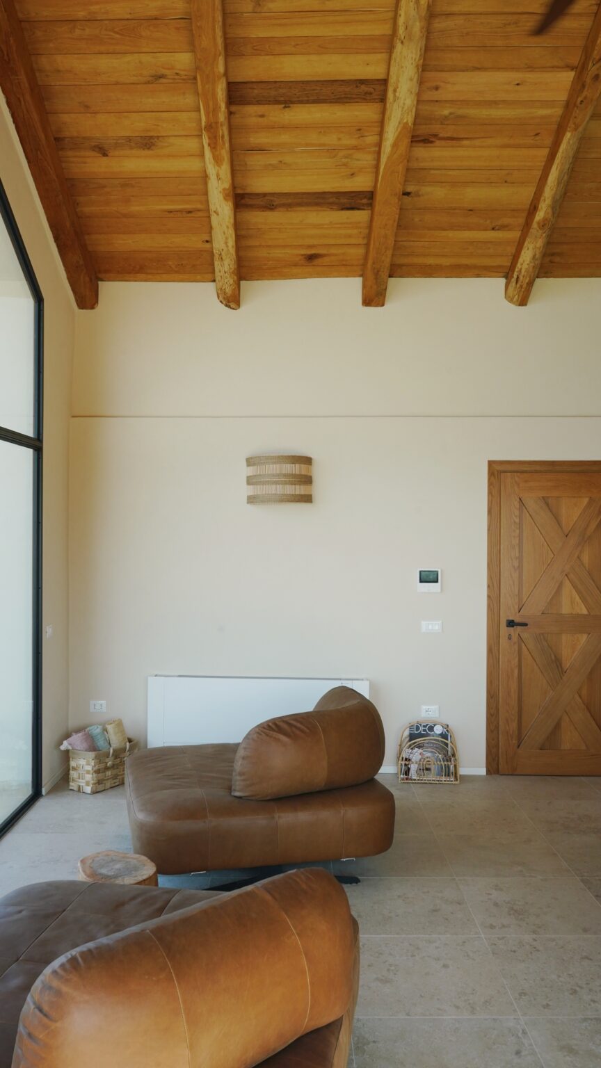 Interior view of a modern living space featuring a textured wall sconce, wooden door, and minimalistic heating unit, highlighting a neutral color palette and contemporary design elements. | Only on SopranoVillas