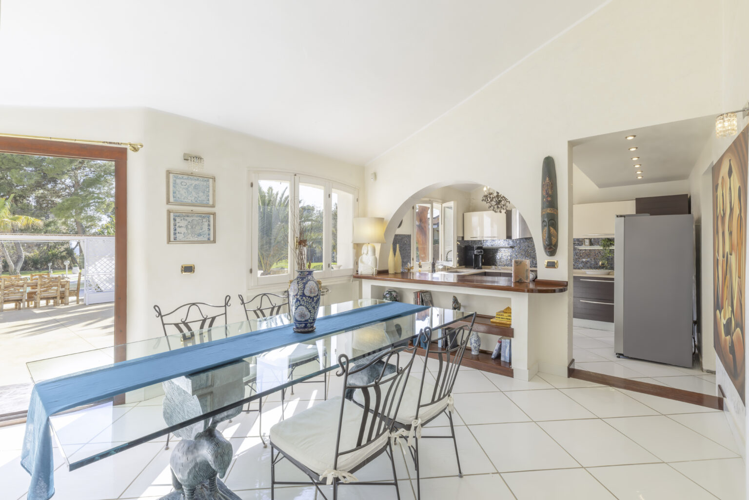 Bright and airy dining area featuring a glass table with black metal chairs, a spacious open layout, and large windows that invite natural light. The room includes modern decor and a view of the outdoor space. | Only on SopranoVillas