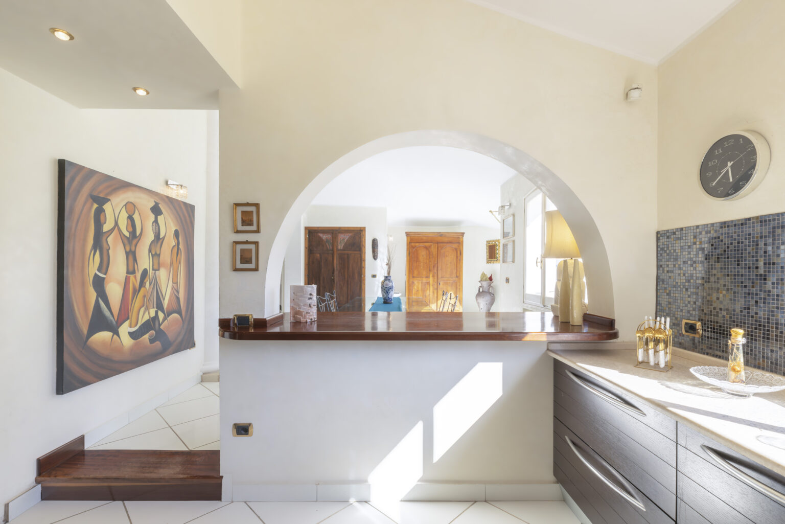 Modern interior design of a stylish kitchen with an arched entryway, featuring a wooden countertop, decorative artwork on the wall, and elegant lighting. | Only on SopranoVillas
