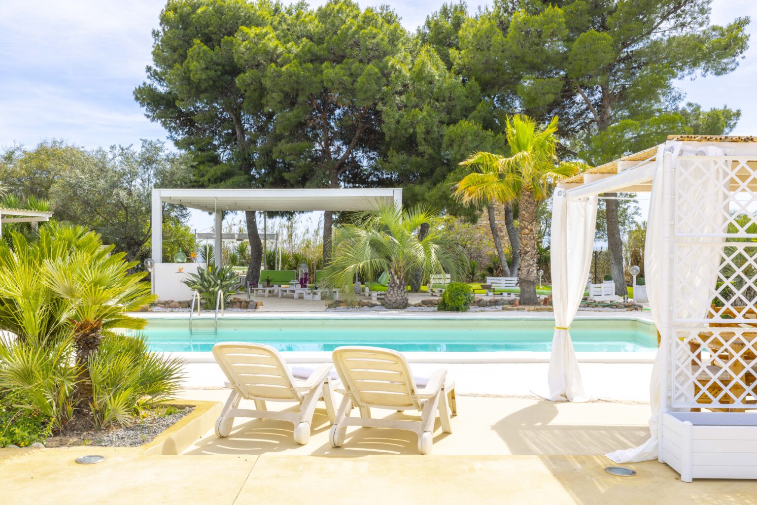 Luxurious backyard oasis featuring a swimming pool, comfortable lounge chairs, and lush greenery, including palm trees and other tropical plants, perfect for relaxation and outdoor gatherings. | Only on SopranoVillas