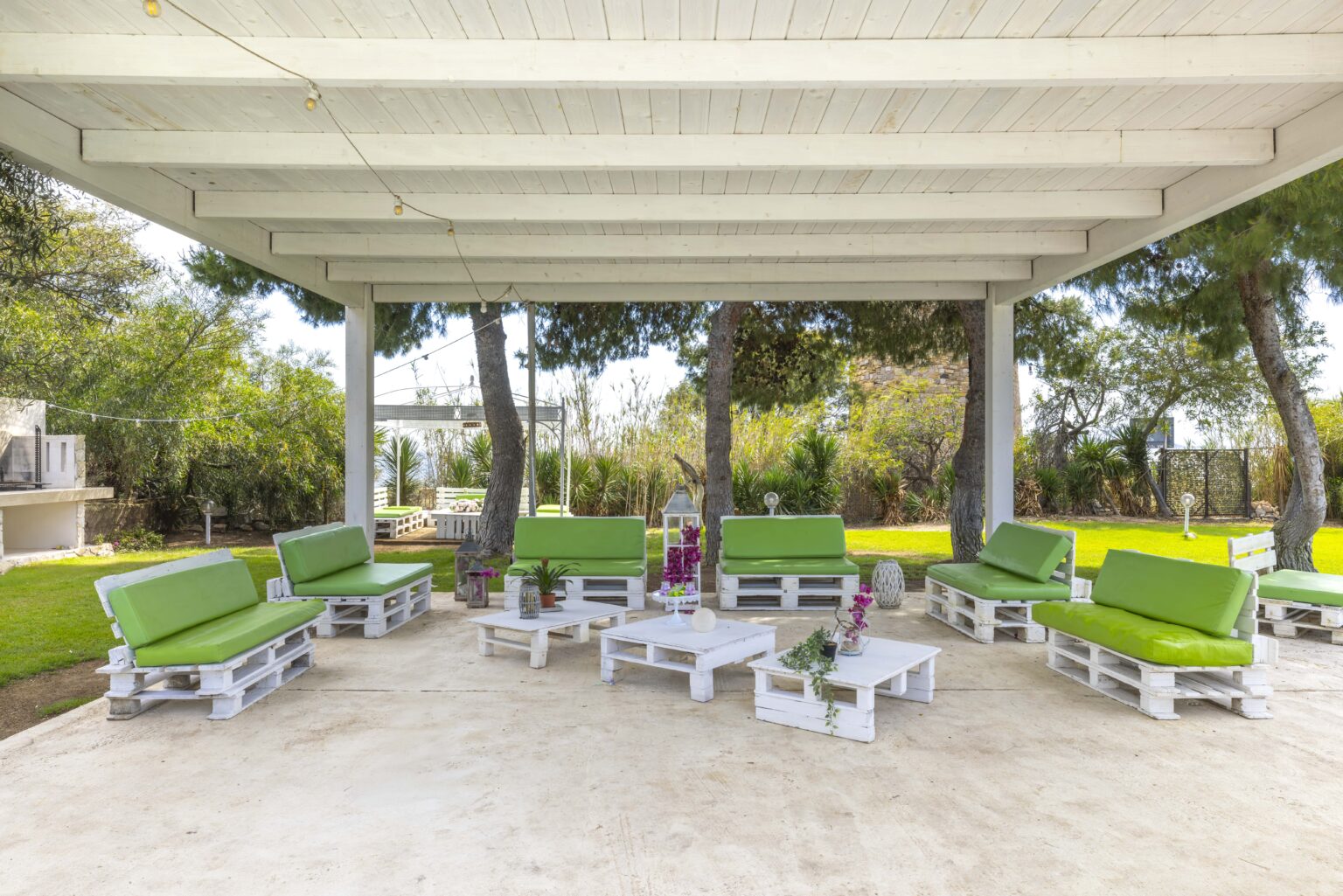 Outdoor lounge area featuring green seating and white tables under a shaded pergola, surrounded by trees and greenery, ideal for relaxation and social gatherings. | Only on SopranoVillas