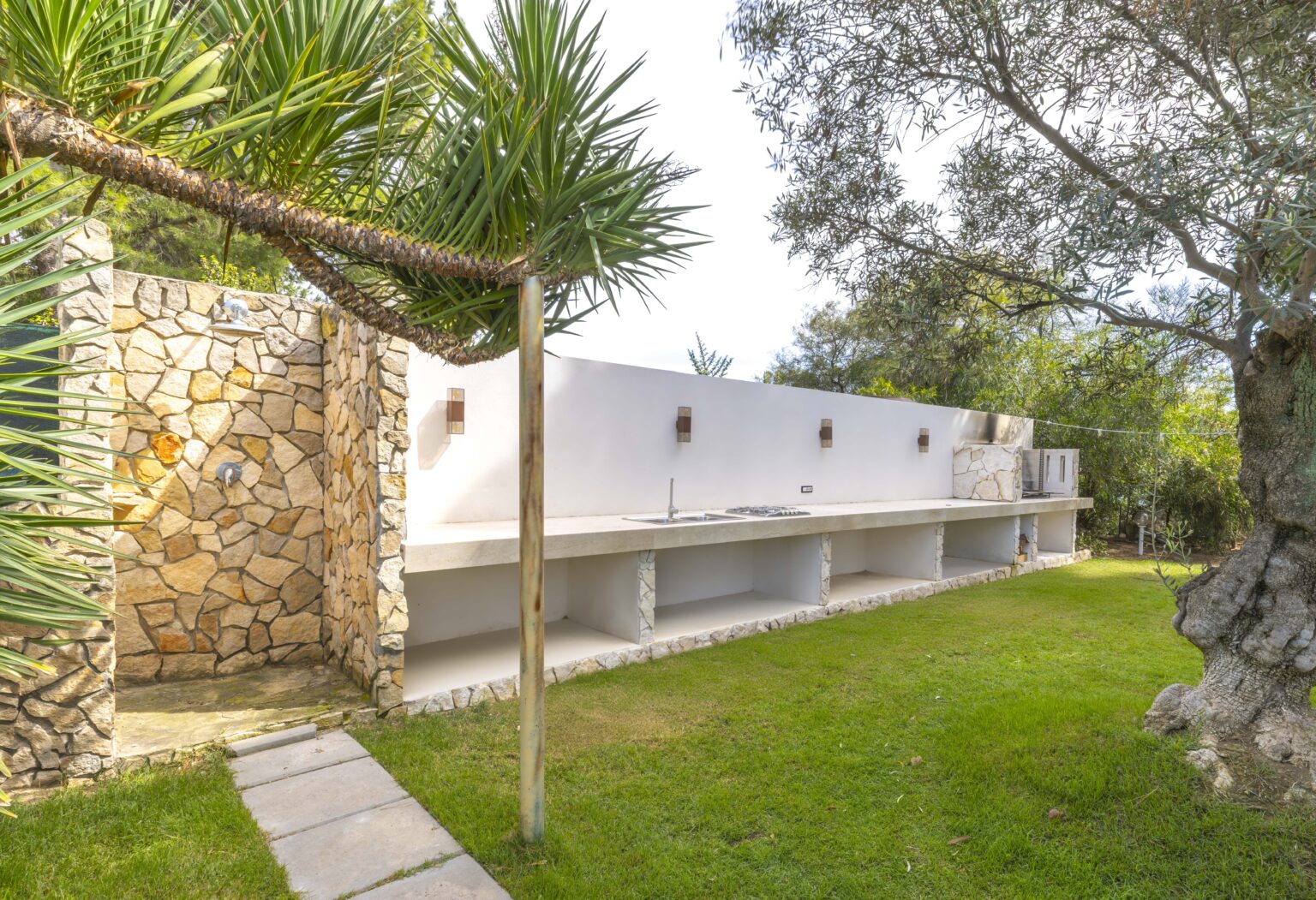 Modern outdoor space featuring a stone wall, white stucco structure, and lush greenery, ideal for relaxation and entertaining. | Only on SopranoVillas