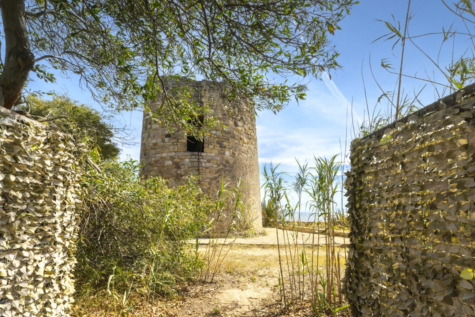 Historic stone tower surrounded by lush greenery and remnants of a stone wall under a clear blue sky. The scene captures the rustic charm and natural beauty of the area. | Only on SopranoVillas