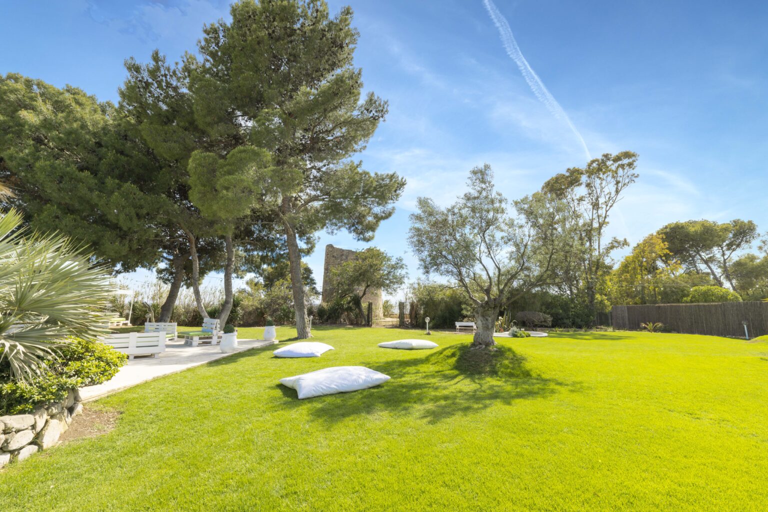 Lush green backyard with trees, outdoor seating area, and decorative cushions on the grass under a clear blue sky. | Only on SopranoVillas