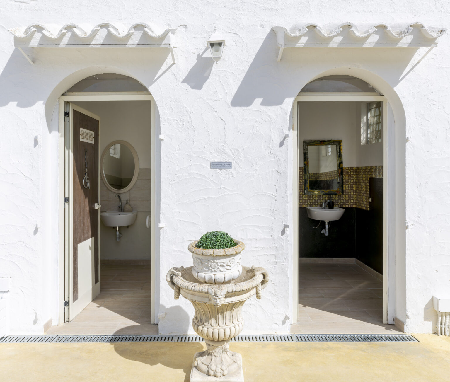 Elegant restroom entrance with arched doorways, featuring a decorative plant pot and stylish interior design elements. Ideal for showcasing modern bathroom aesthetics. | Only on SopranoVillas