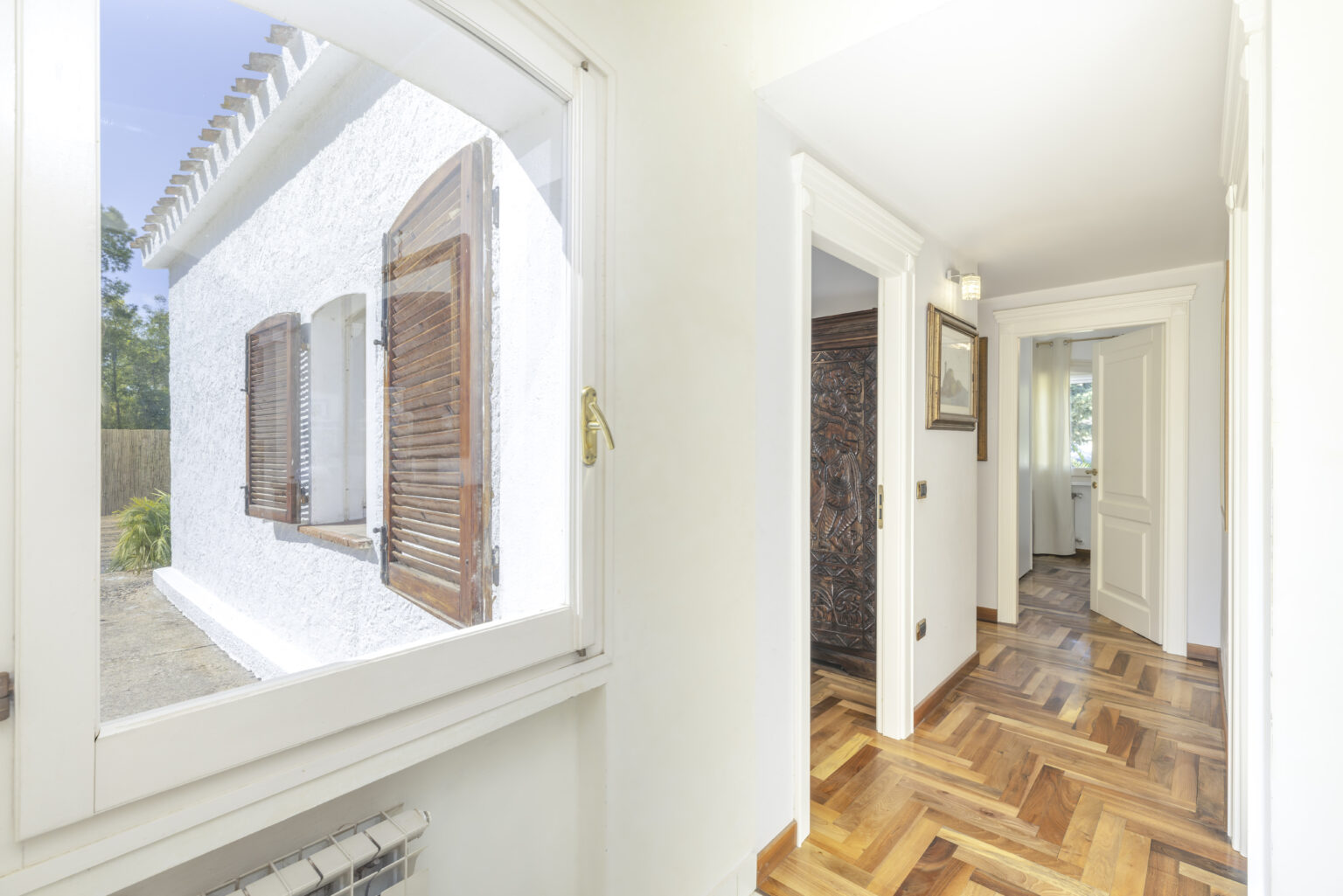 Bright and airy hallway with wooden flooring, showcasing a view of an exterior window with wooden shutters and doorways leading to other rooms. | Only on SopranoVillas