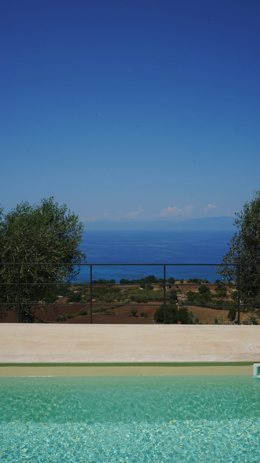 Scenic coastal view featuring a clear blue sea and distant mountains, framed by olive trees and a metal railing, ideal for travel and nature enthusiasts. | Only on SopranoVillas