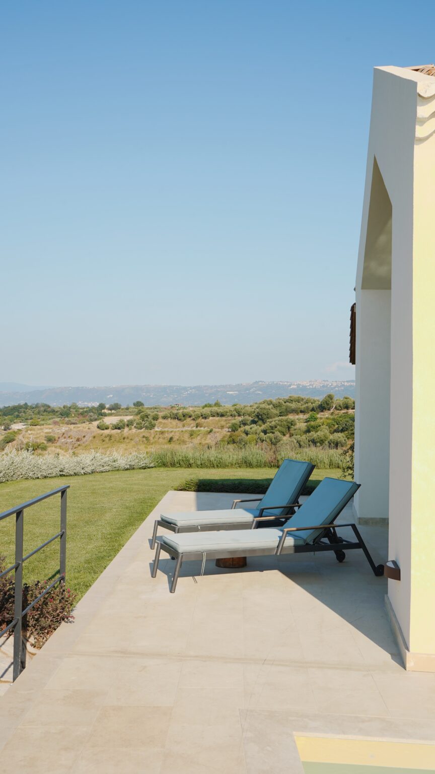 Lounge chairs on a patio overlooking a scenic landscape with rolling hills and clear blue skies, ideal for relaxation and outdoor enjoyment. | Only on SopranoVillas