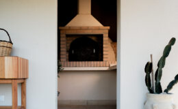 Cozy outdoor space featuring a rustic brick pizza oven, with a wooden table and potted cactus in the foreground. Ideal for alfresco dining and entertaining.