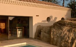 Modern villa with a swimming pool and natural rock features, showcasing minimalist architecture and warm sunset lighting.