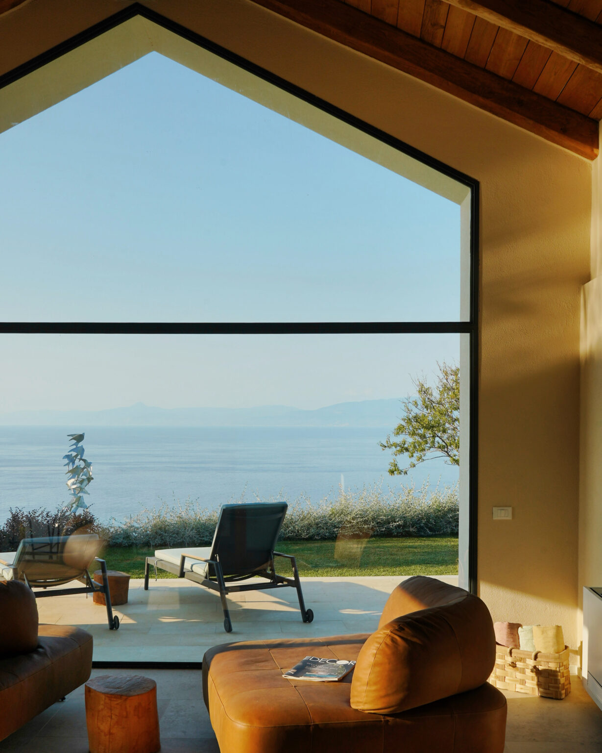 Modern living room with large window showcasing a serene ocean view and lush greenery, perfect for relaxation and enjoying nature. | Only on SopranoVillas
