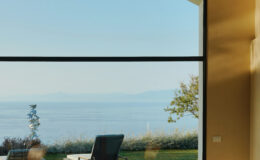 Modern living room with large window showcasing a serene ocean view and lush greenery, perfect for relaxation and enjoying nature.