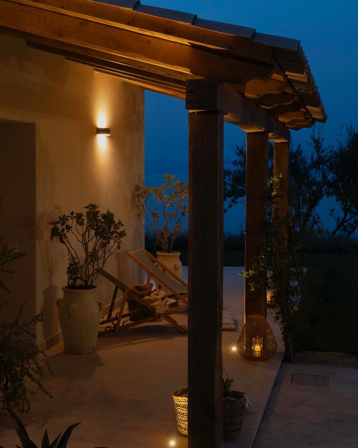 Cozy outdoor patio at dusk featuring wooden pillars, soft lighting, and potted plants, creating a serene ambiance for relaxation. | Only on SopranoVillas