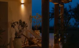 Cozy outdoor patio at dusk featuring wooden pillars, soft lighting, and potted plants, creating a serene ambiance for relaxation.