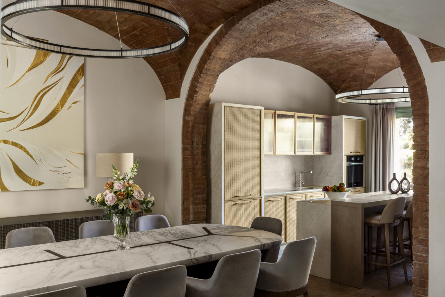 Modern dining room featuring a stylish marble table, elegant chairs, and a floral centerpiece, with a well-designed kitchen in the background. The space showcases arched ceilings and contemporary lighting fixtures, creating a warm and inviting atmosphere. | Only on SopranoVillas
