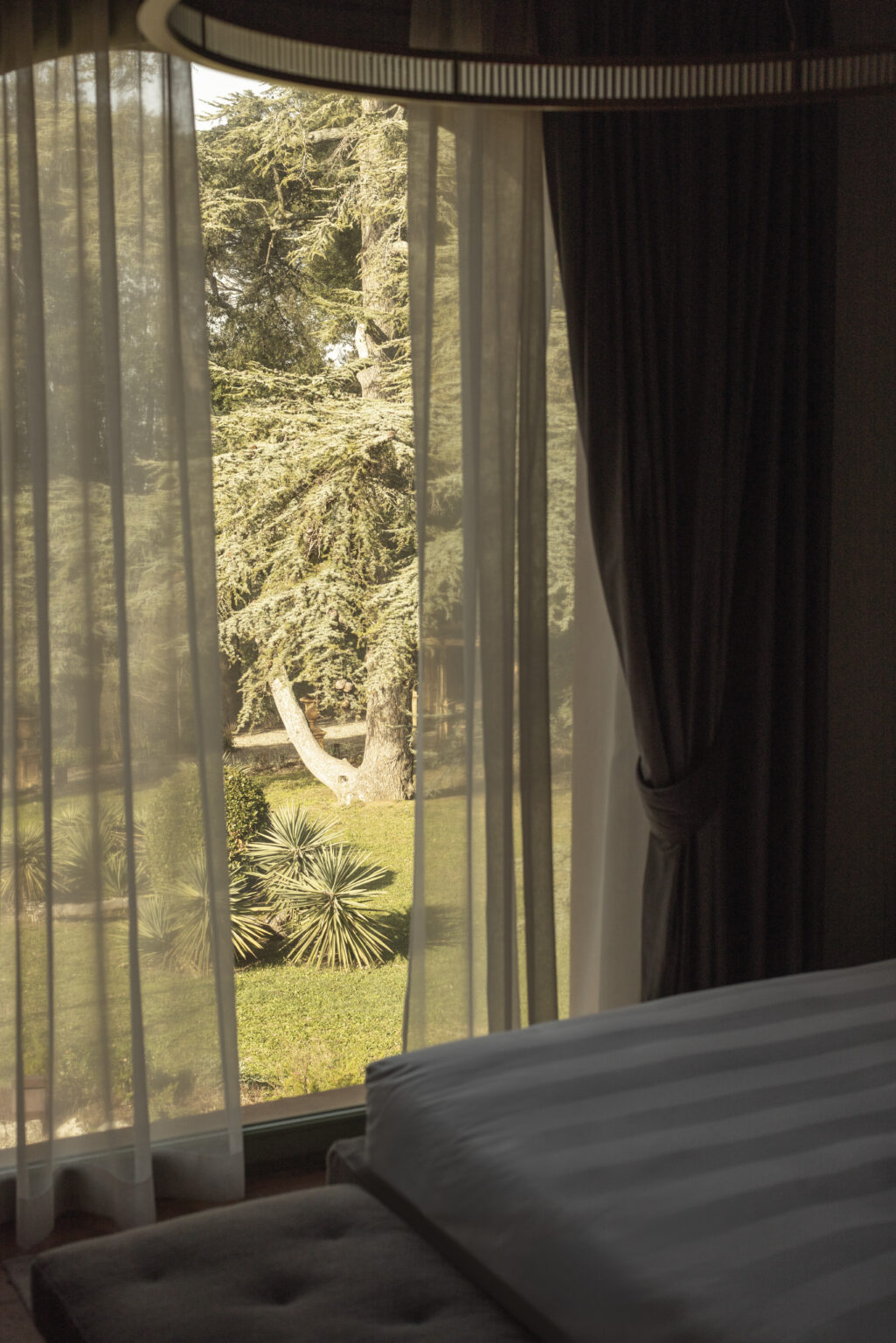 Light filtering through sheer curtains, revealing a lush garden with trees and palm plants outside a window. | Only on SopranoVillas