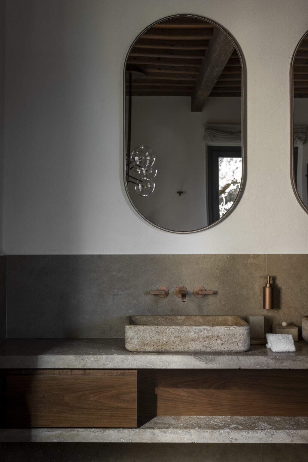 Modern bathroom design featuring two round mirrors above a stylish sink with copper fixtures, complemented by a sleek stone wall. The soft lighting enhances the contemporary aesthetic. | Only on SopranoVillas
